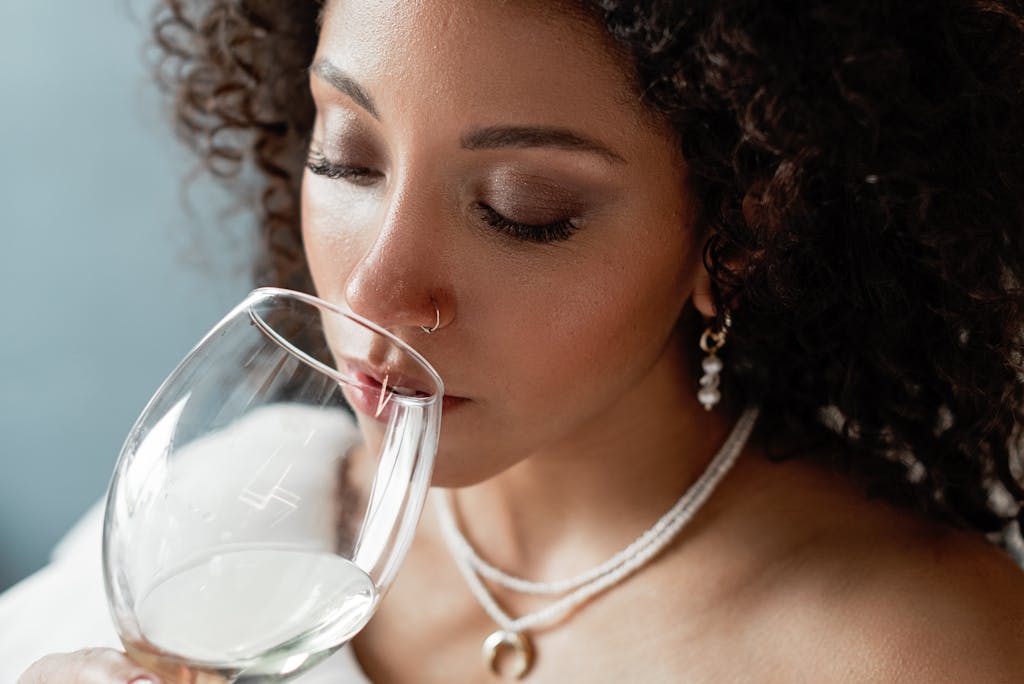 Close-up portrait of a black woman savoring a glass of white wine, eyes closed, exuding grace and beauty.